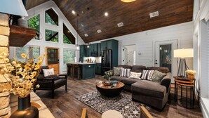 A spacious living area with a large sofa, a coffee table, and a kitchen in the background. - Luna Ridge · New! Cozy Escape: Hot Tub, Fire Pit, King Suite (Broken Bow)