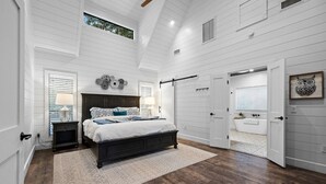 A bedroom with a large bed, a nightstand, a dresser, a walk-in closet, and a bathroom with a bathtub. - Luna Ridge · New! Cozy Escape: Hot Tub, Fire Pit, King Suite (Broken Bow)