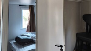 Een kamer met een bed, een stoel, een airconditioning en een deur naar een andere kamer.