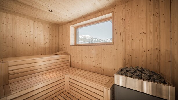 A sauna room with wooden walls, a bench, a window, and a stone-filled sauna heater. - Luxury Chalet in Bichlbach (Bichlbach)