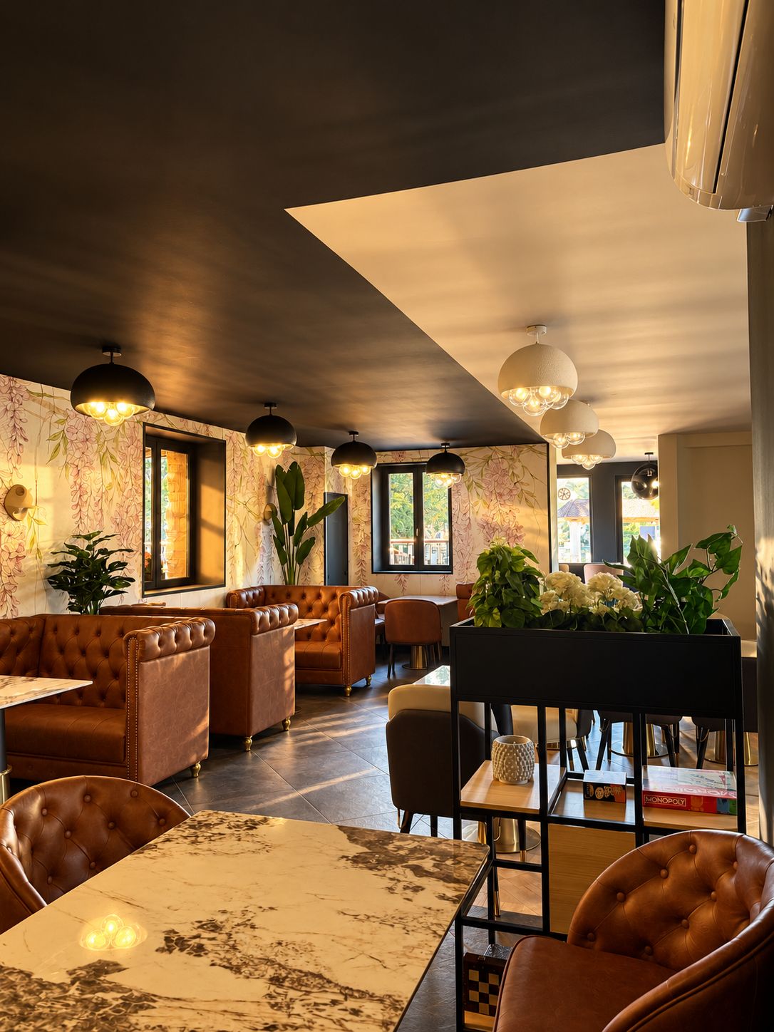 Interior de restaurante com assentos de couro, mesas de mármore e iluminação pendente.