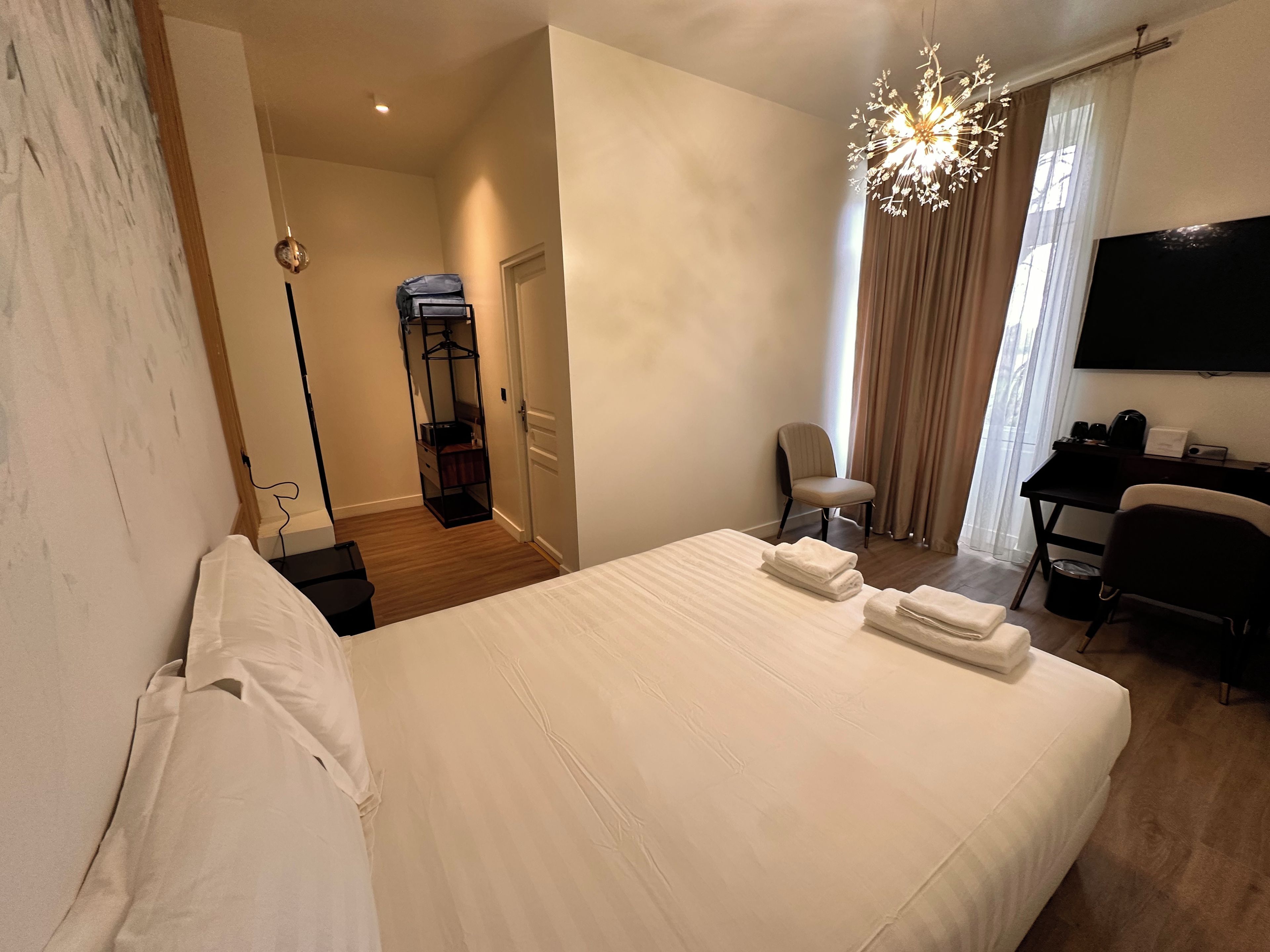 A hotel room with a bed, a desk with a chair, a television, and a wardrobe.