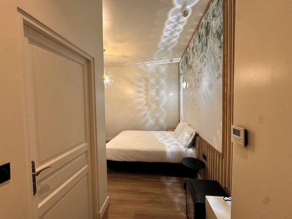 Un dormitorio con cama, mesita de noche, termostato en la pared y lámpara original en el techo.