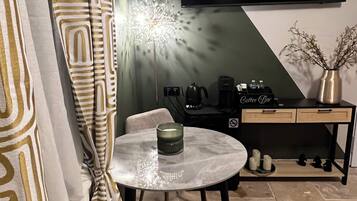 Una sala de estar moderna con un televisor de pantalla plana montado en la pared, una mesa redonda de vidrio con una vela, un sofá y una estación de café con una cafetera y tazas.
