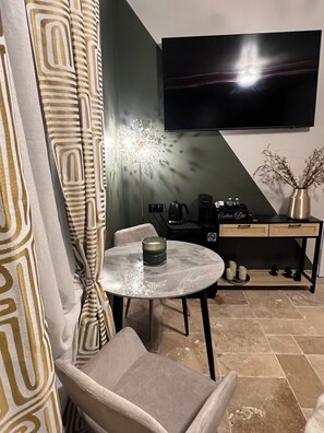 Una sala de estar moderna con un televisor de pantalla plana montado en la pared, una mesa redonda de vidrio con una vela, un sofá y una estación de café con una cafetera y tazas.