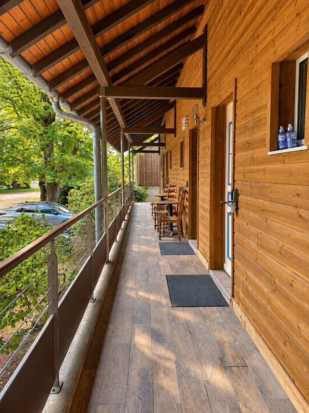 A covered wooden building with a balcony, outdoor seating, and a view of greenery.