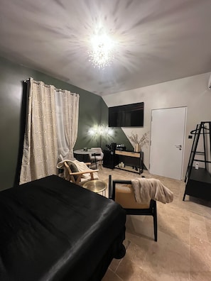 Un dormitorio con cama, una silla, escritorio, televisor y una puerta.