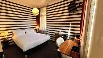 Une chambre d’hôtel équipée d’un lit, d’une table de chevet, d’une lampe, d’un bureau, d’une chaise et d’un téléviseur fixé au mur.