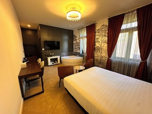 Ein Hotelzimmer mit Bett, Schreibtisch, Stuhl, Fernseher, Badewanne und einem fenster mit Vorhängen.