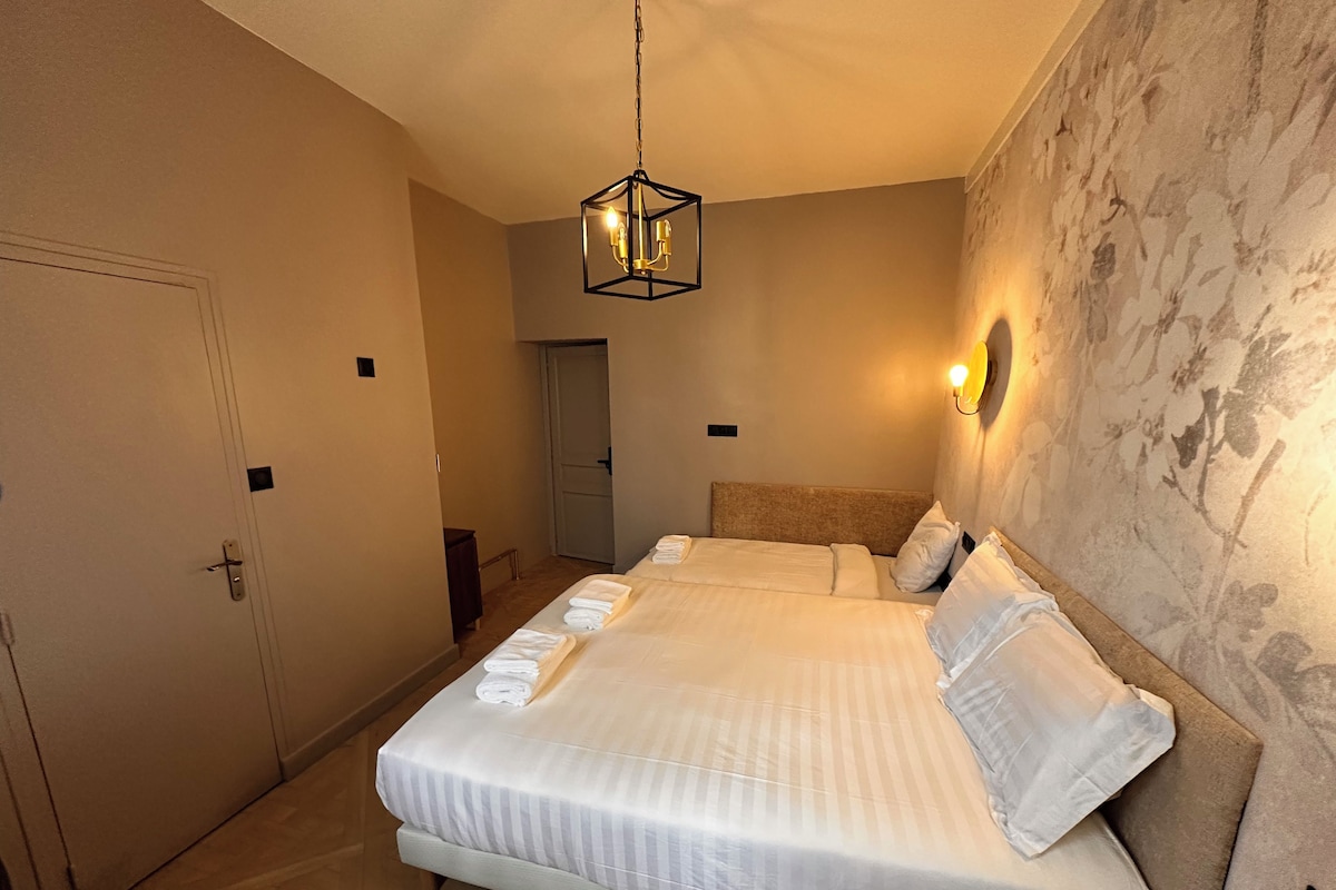 Ein Hotelzimmer mit einem großen Bett, einer Hängelampe, einer Tür und einer Wand mit einem Blumenmuster.