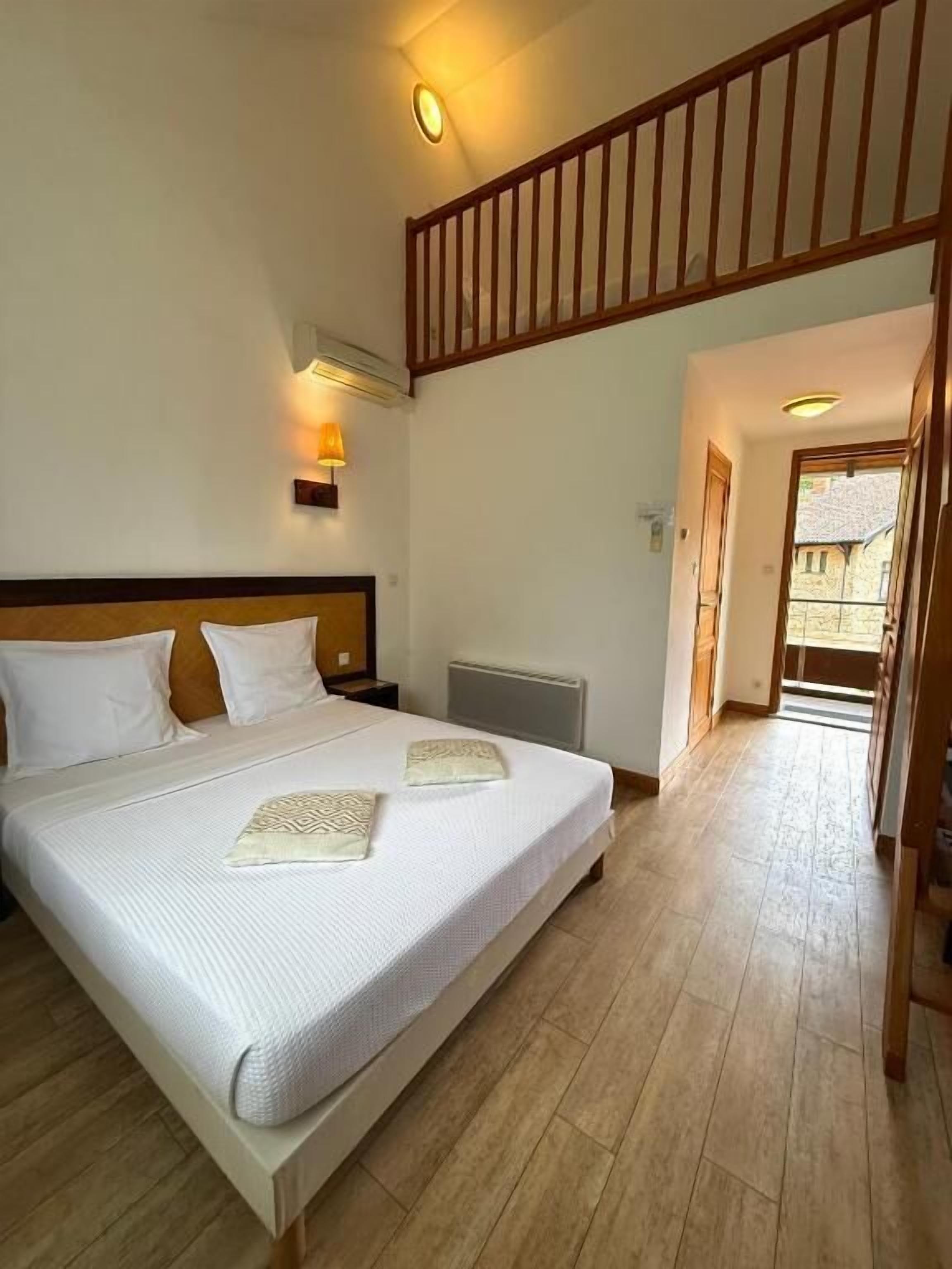 A bedroom with a large bed, a wooden headboard, an air conditioning unit, and a staircase leading to an upper level.
