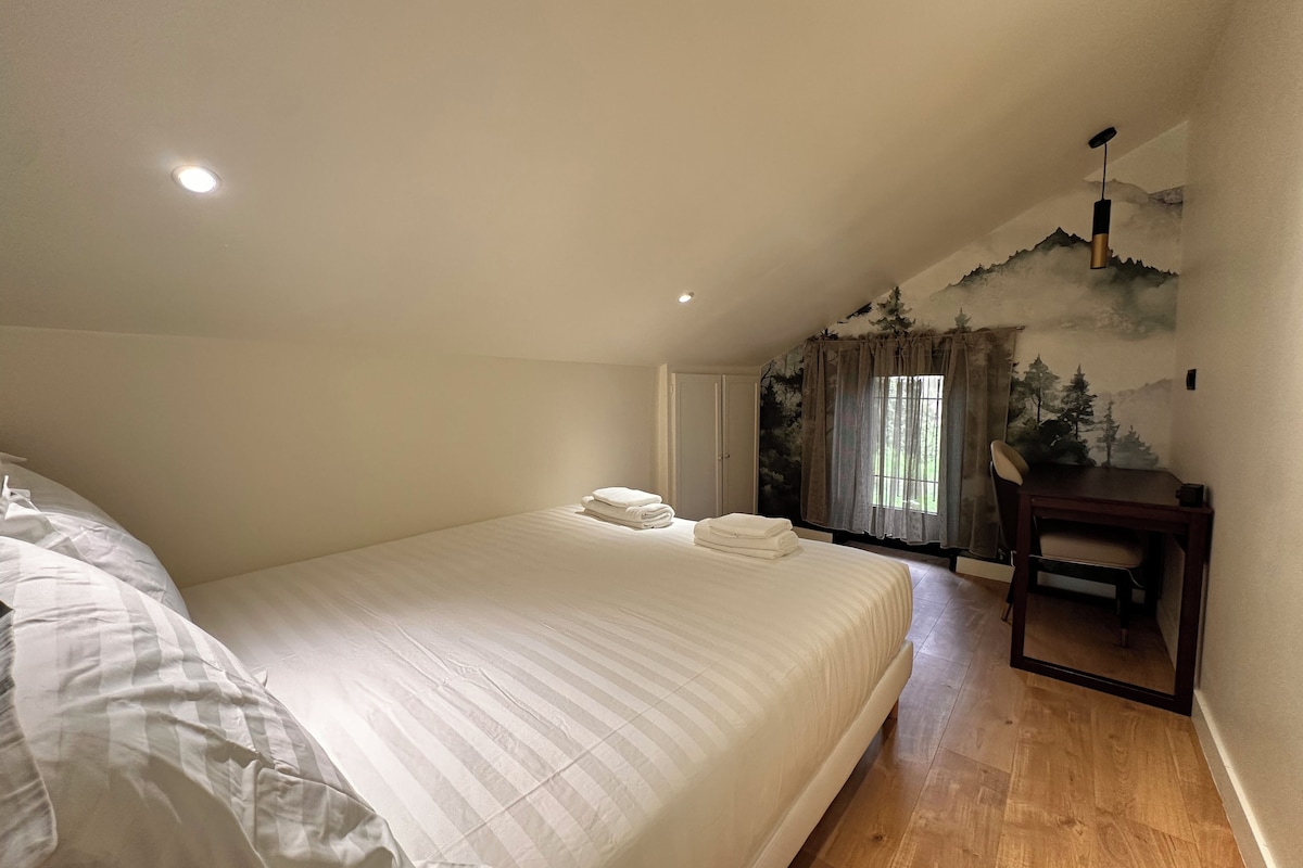 Ein Schlafzimmer mit einem großen Bett, einem Schreibtisch, einem Stuhl und einem Vorhangfenster.