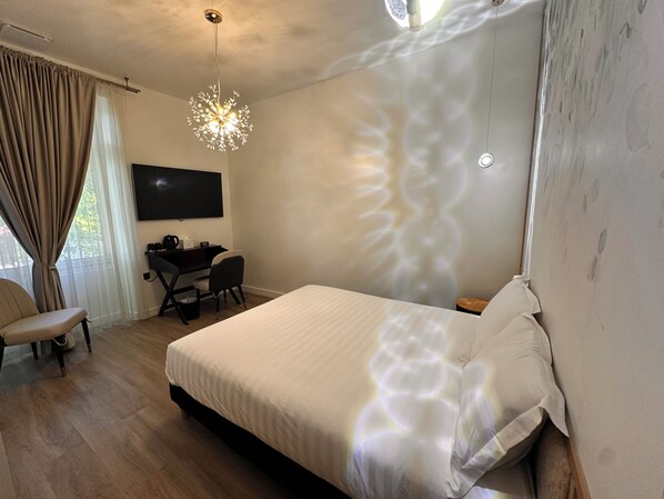 Une chambre d’hôtel comprenant un lit, un bureau avec une chaise, une télévision et un luminaire au plafond original.