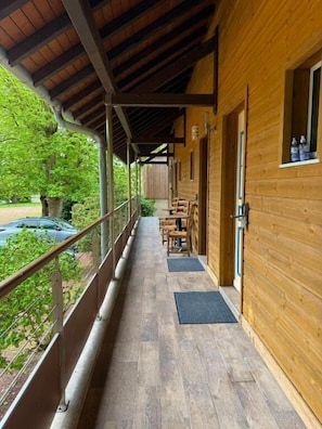 Una cabaña de madera con un porche cubierto, mobiliario exterior y vistas de la vegetación circundante.