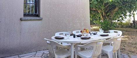A patio table set with white plastic chairs, a bowl of fruit, and a bottle of water.