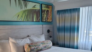 A hotel room with a large bed, a nightstand, a wall-mounted lamp, and a window with curtains.