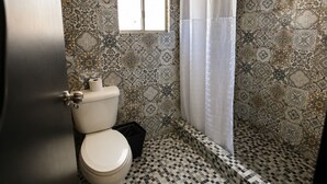 A bathroom with a toilet, a shower with a curtain, and patterned tiles. - Maviri Hotel (Tijuana)