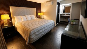 A hotel room with a large bed, two bedside lamps, a flat-screen TV, a small desk with a plant, and a bathroom visible through an open door. - Maviri Hotel (Tijuana)