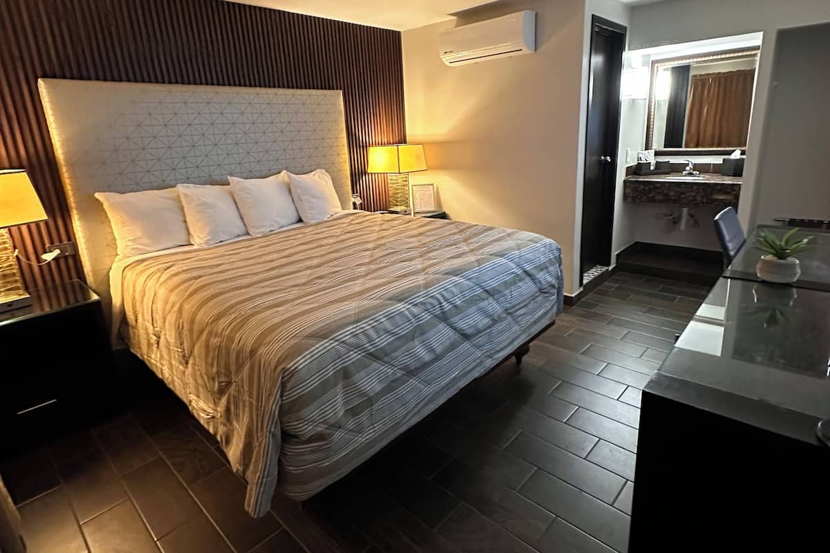 Hotellihuone, jossa on suuri sänky, yöpöydät, työpöytä ja peili.