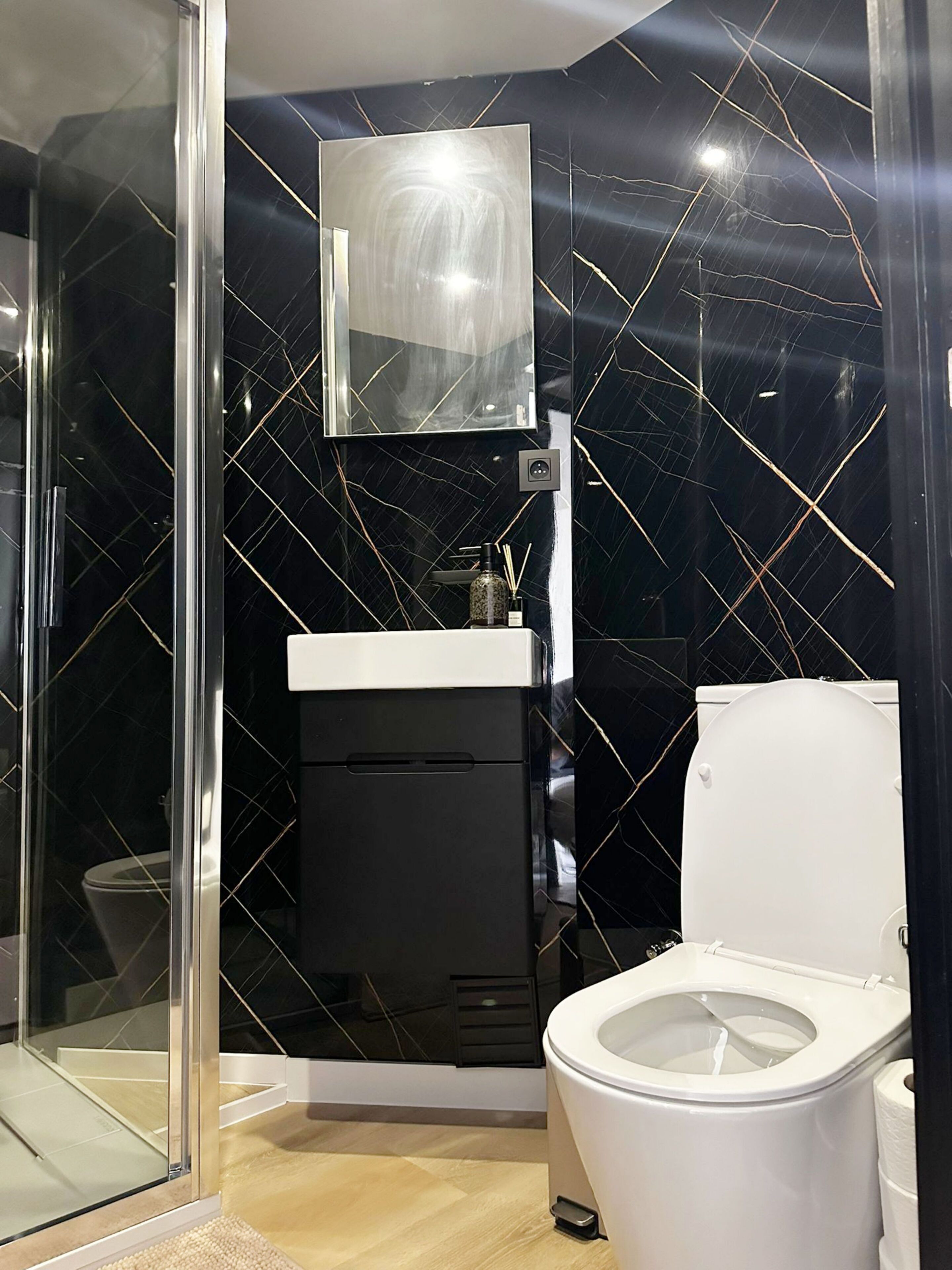 Un baño moderno con cabina de ducha de vidrio, inodoro blanco, lavamanos negro y espejo sobre el lavamanos.