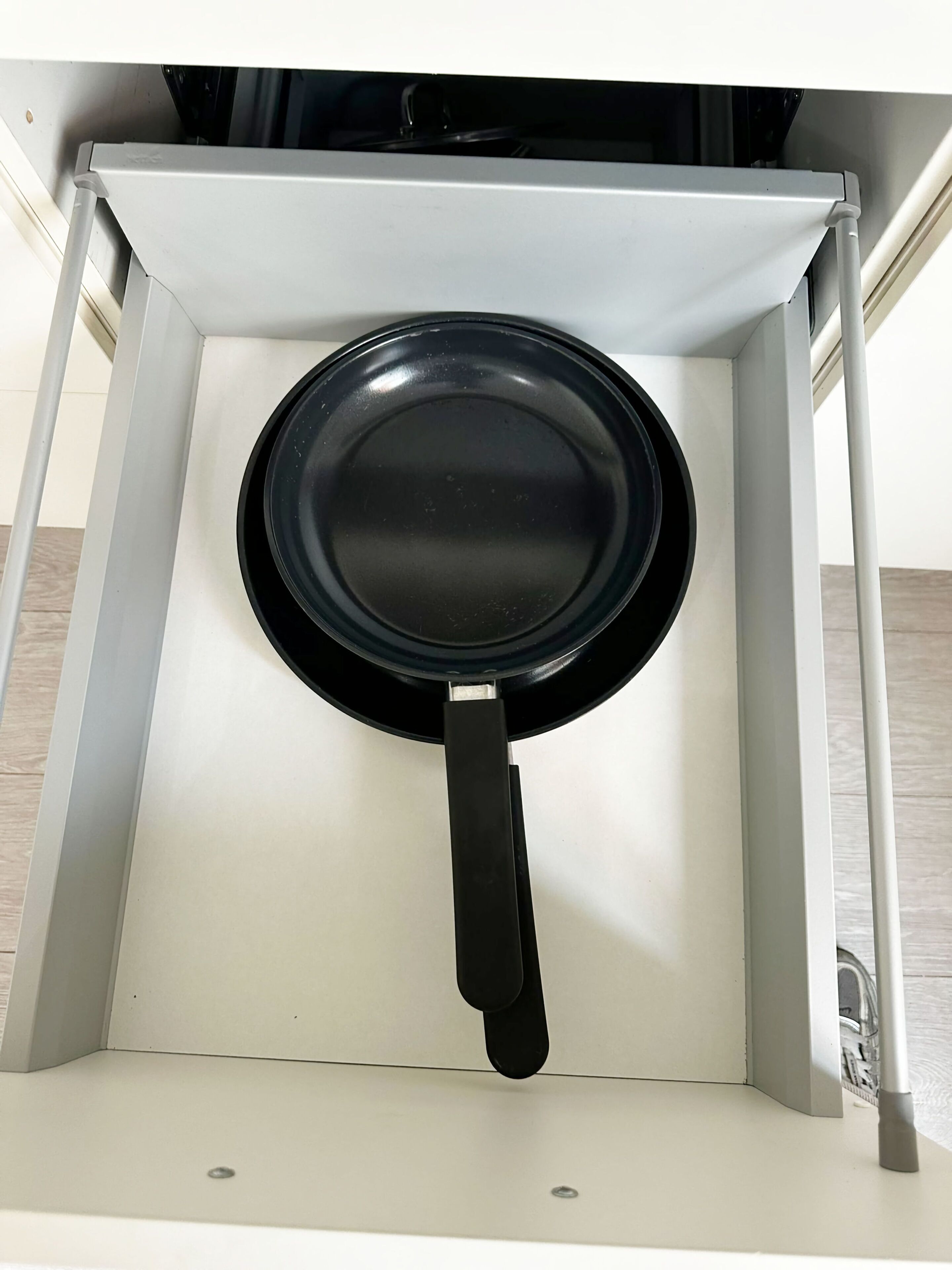 A kitchen cabinet with a black frying pan hanging inside.