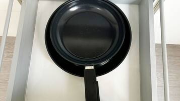 A kitchen cabinet with a black frying pan hanging inside.