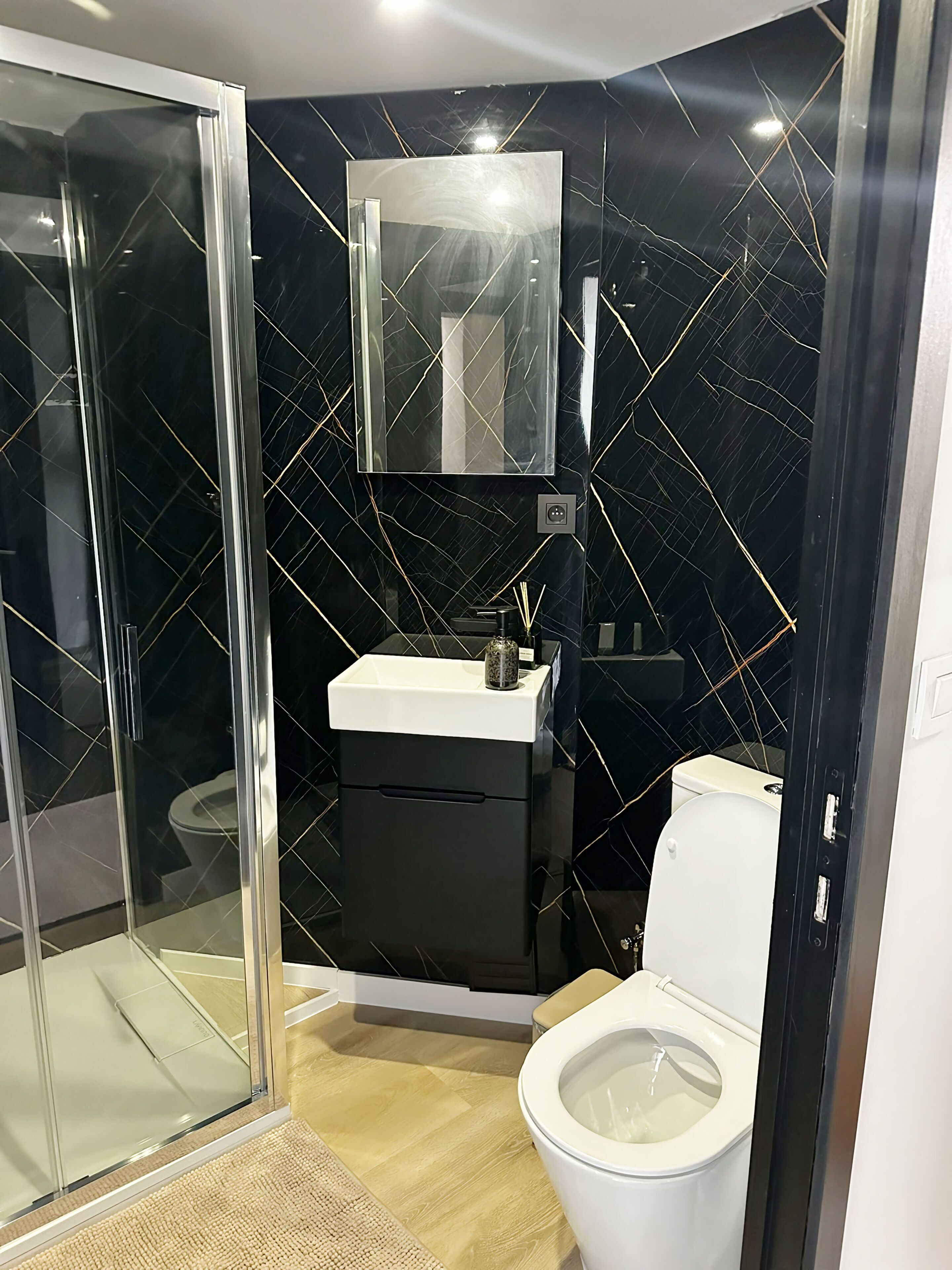 Un bagno moderno con box doccia in vetro, un water bianco e un mobile lavabo nero con specchio.
