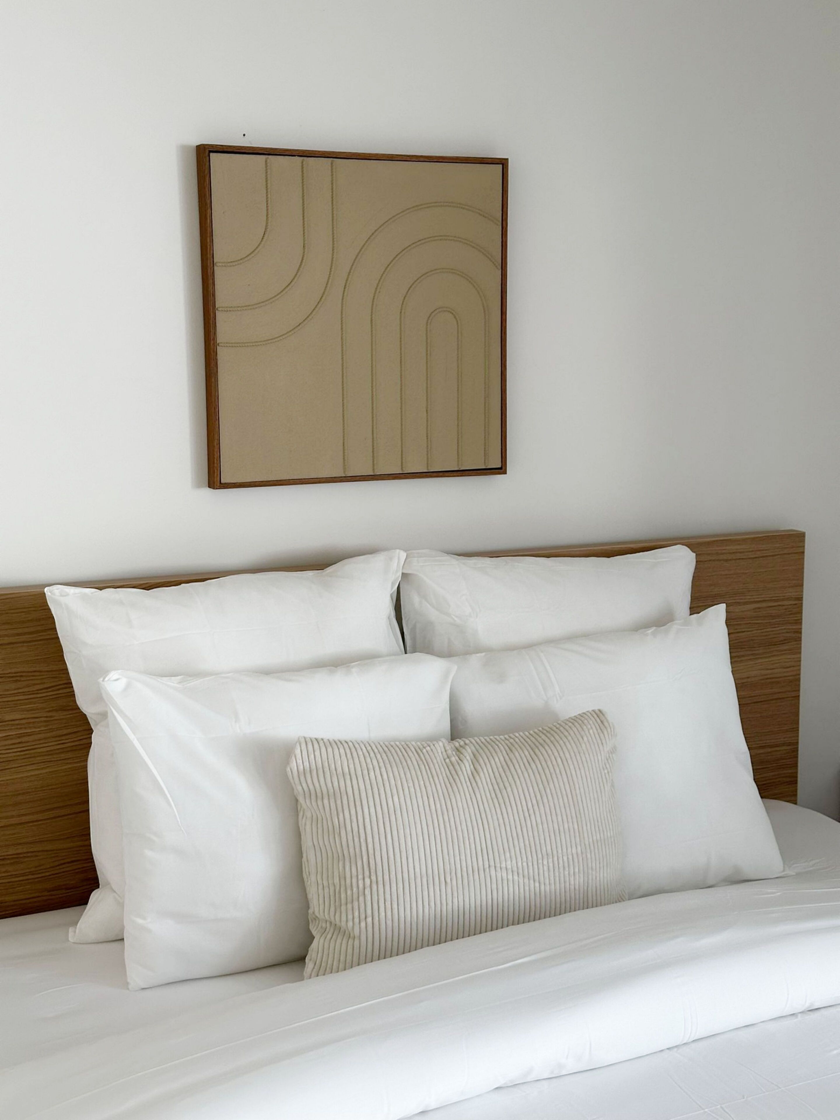 Una cama con ropa blanca y almohadas, un cabecero de madera y una obra de arte abstracta colgada en la pared.
