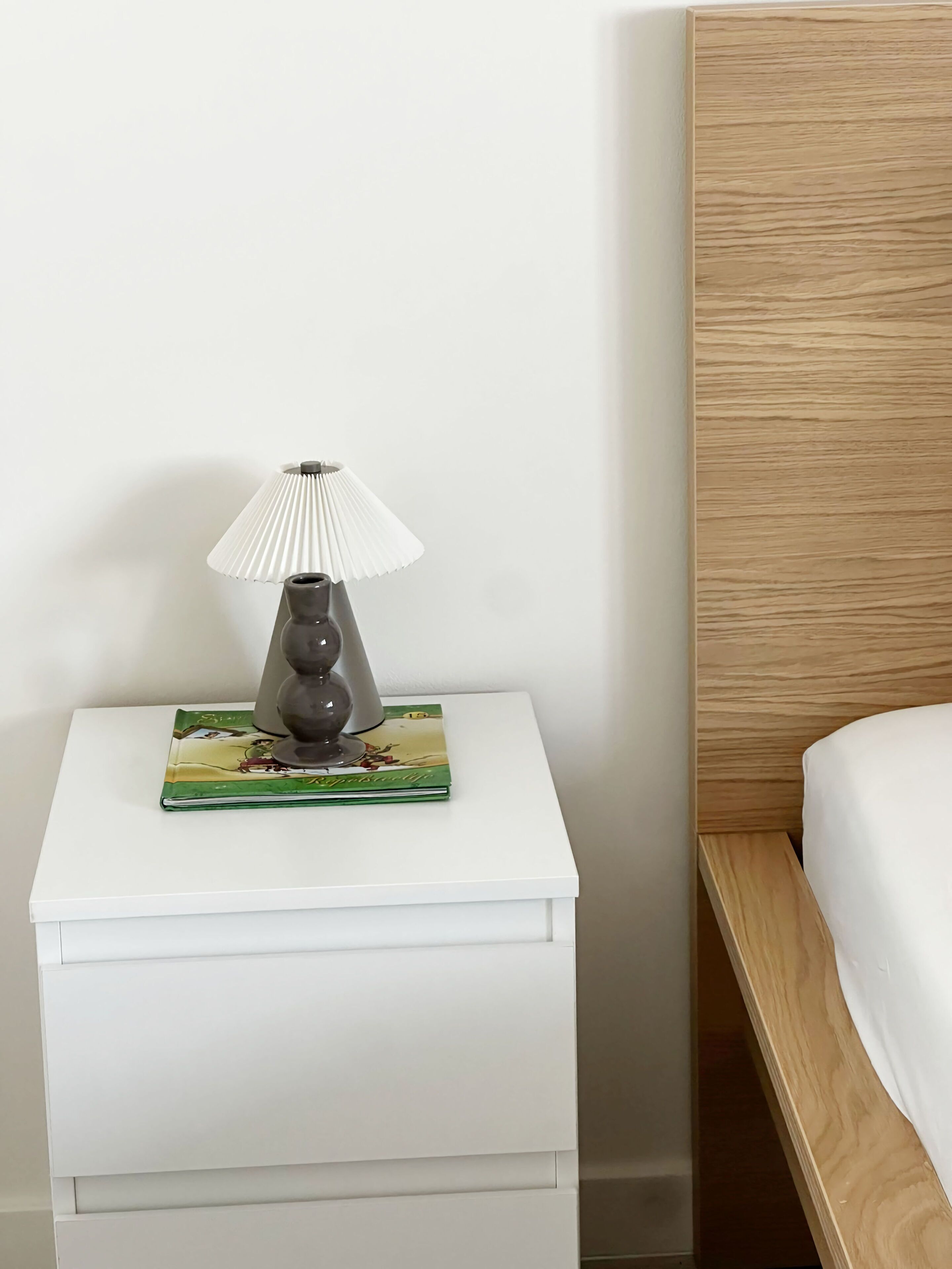 Un comodino bianco con una lampada e un libro.