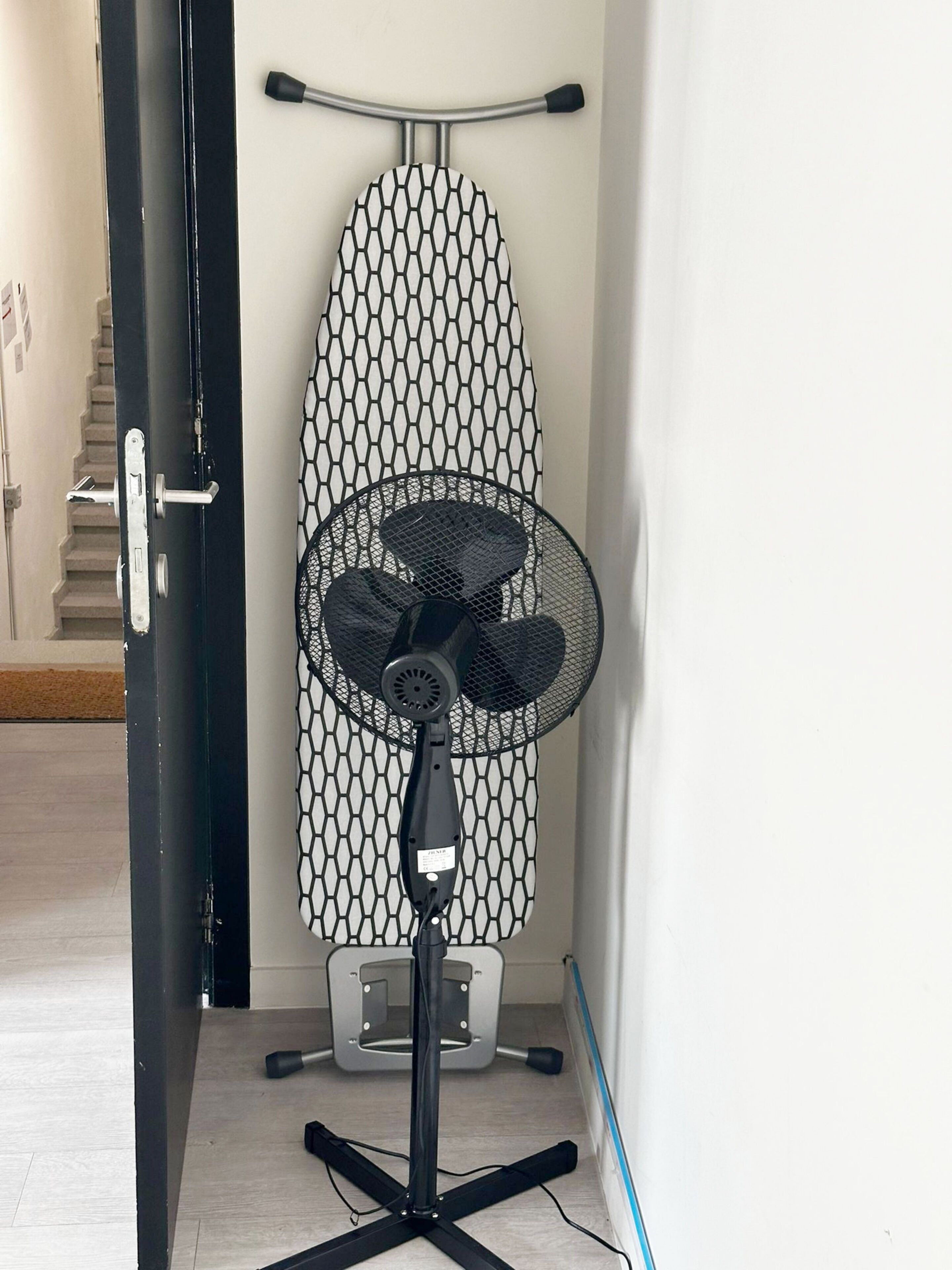 En gulvventilator med et gitterdesign, et vægmonteret strygebræt og en dør med håndtag.