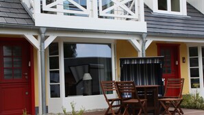 A two-story building with a patio area featuring a table and chairs, large windows, and a red door. - Apartment mit Strandkorb und Terrasse in Uckeritz (Ueckeritz)