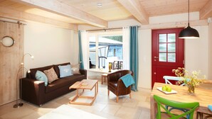 A living room with a brown sofa, a wooden coffee table, a dining table with chairs, and a red door. - Apartment mit Strandkorb und Terrasse in Uckeritz (Ueckeritz)