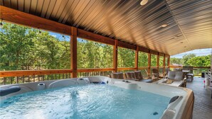 A hot tub area with a wooden deck, outdoor furniture, and a view of trees. - Lumberjack Lodge with Amenities (Hollister)
