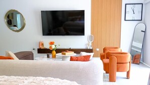 A modern hotel room with a large bed, a flat-screen TV, a round mirror, an orange armchair, and a wooden panel wall. - Newly Built Apartment in the Heart of Ocho Rios (Ocho Rios)