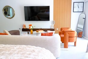 A modern hotel room with a large bed, a flat-screen TV, a round mirror, an orange armchair, and a wooden panel wall. - Newly Built Apartment in the Heart of Ocho Rios (Ocho Rios)