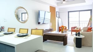 A modern living room with a dining area, a flat-screen TV, a large window, and a balcony. - Newly Built Apartment in the Heart of Ocho Rios (Ocho Rios)