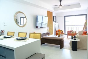 A modern living room with a dining area, a flat-screen TV, a large window, and a balcony. - Newly Built Apartment in the Heart of Ocho Rios (Ocho Rios)