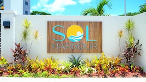 A sign with 'SOL HARBOUR' and a logo, surrounded by various plants. - Newly Built Apartment in the Heart of Ocho Rios (Ocho Rios)