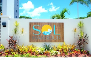 A sign with 'SOL HARBOUR' and a logo, surrounded by various plants. - Newly Built Apartment in the Heart of Ocho Rios (Ocho Rios)