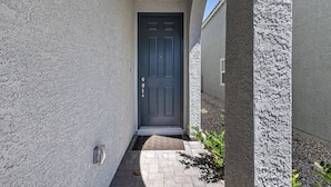 Un étroit sentier mène à une porte sombre, avec un mur à texture sur un côté et une colonne de l’autre.