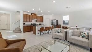 Une cuisine moderne avec des meubles en bois, un îlot central doté de chaises, un coin repas avec un canapé et une table basse, et un escalier menant à un autre niveau.