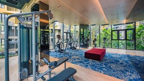 Een sportschool met trainingsapparatuur, een rode bank en grote ramen met uitzicht op groen.