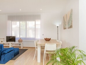 A modern living room with a TV, sofa, dining table, chairs, and a large window. - Matilde by Interhome (St Antoni de Calonge)