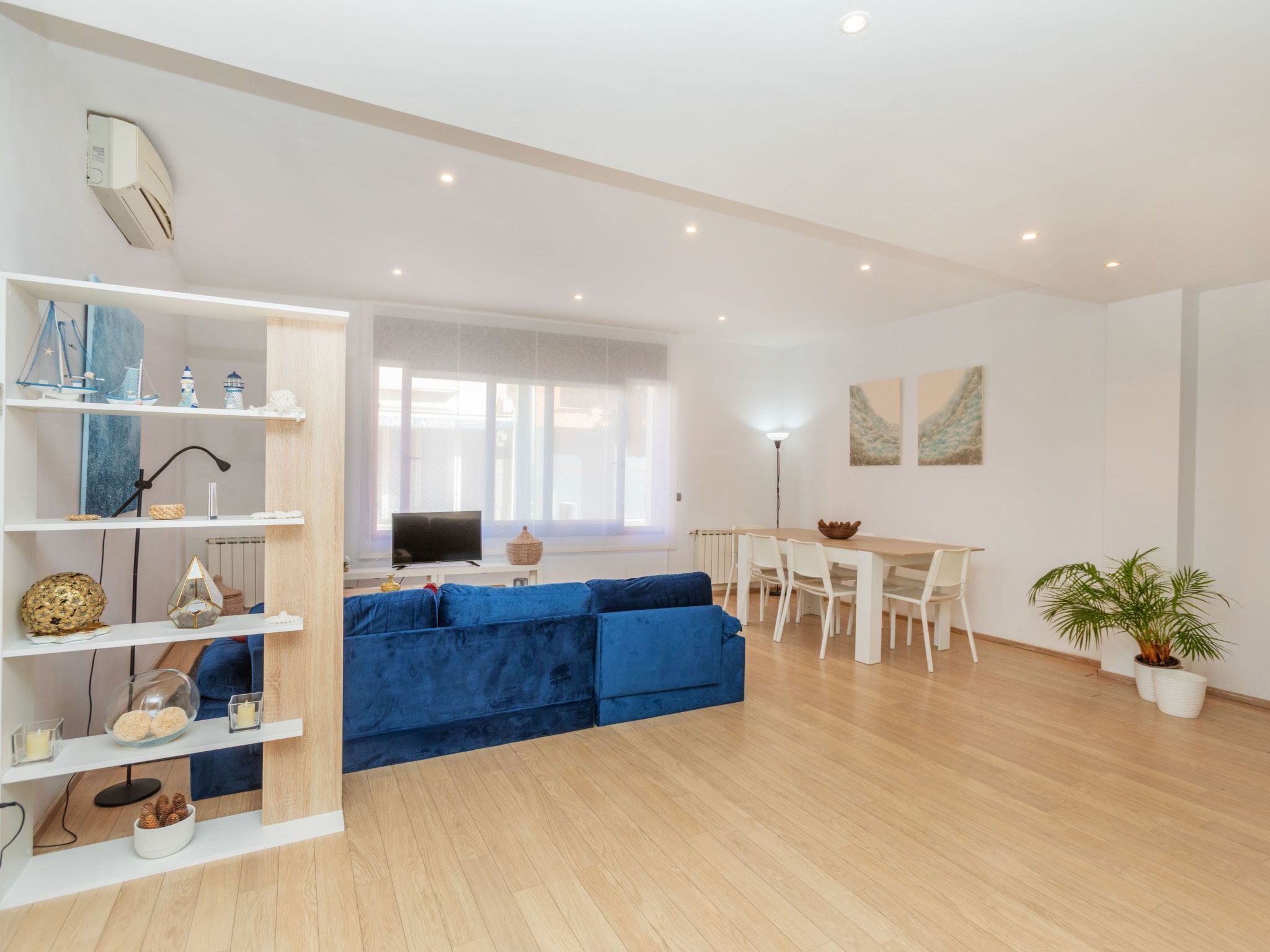 A modern living room with a blue sofa, a dining area with a table and chairs, and a kitchen in the background.
