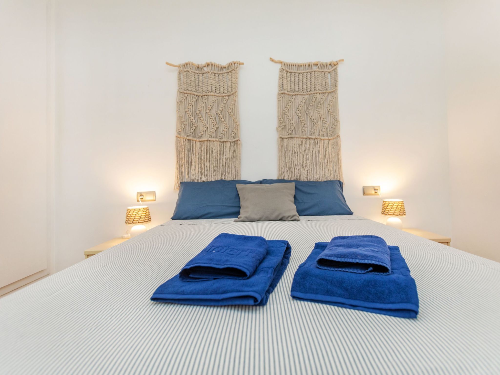Ein Bett mit zwei blauen Handtüchern, einer gestreiften Bettdecke und zwei an der Wand befestigten Wandteppichen aus Makramee.