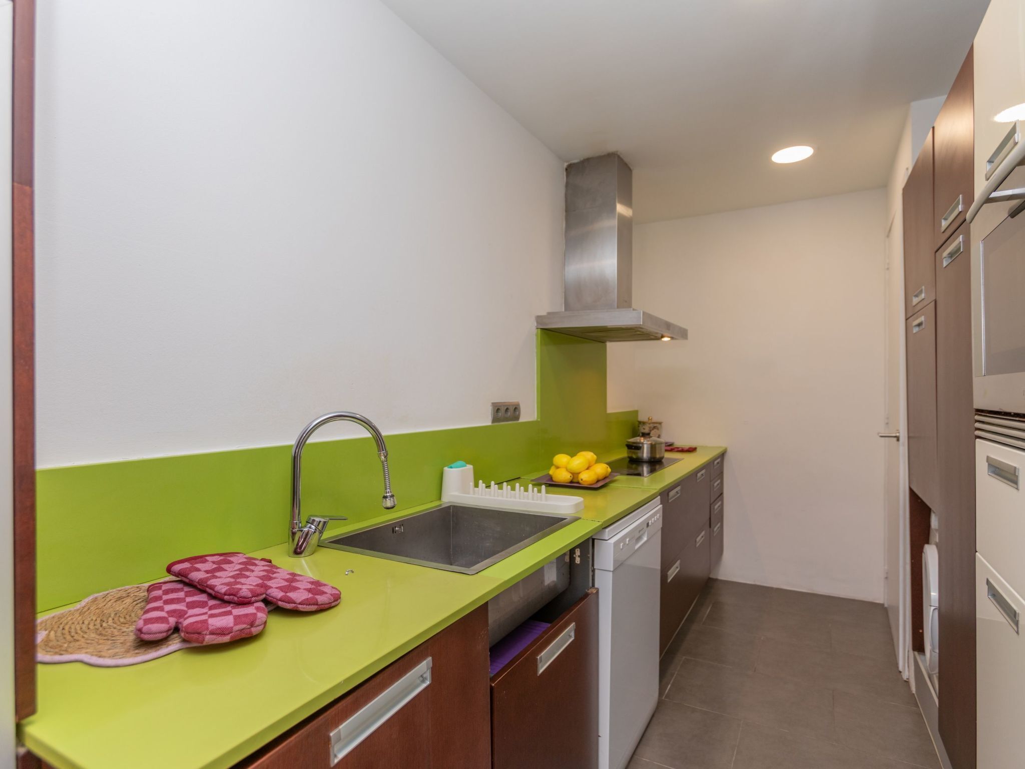 Uma cozinha compacta com bancada verde, pia de aço inoxidável e máquina de lavar louça.
