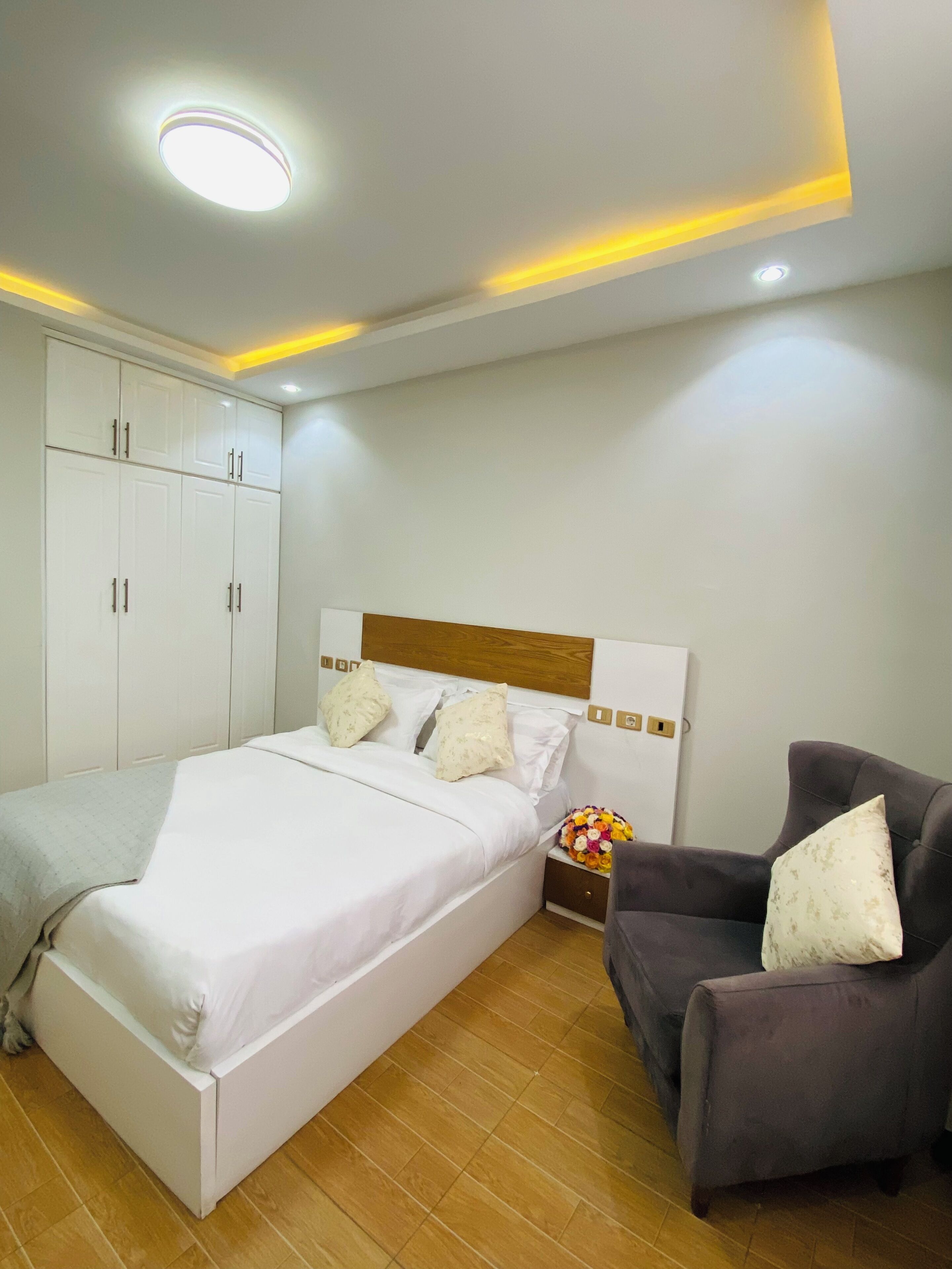 Een slaapkamer met een bed, nachtkastje, stoel en een kledingkast.