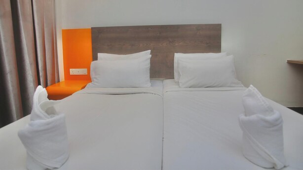 Cama doble con ropa de cama blanca, cabecera de madera y pared de acento naranja.