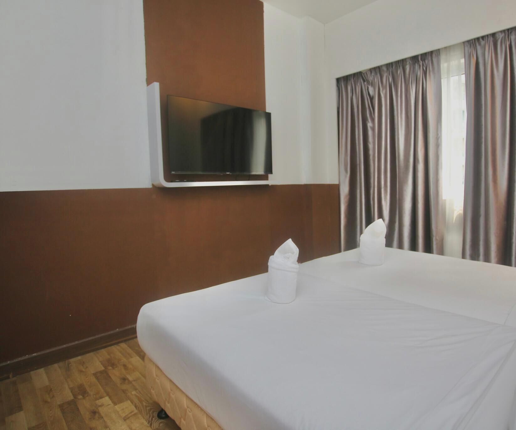 Ein Hotelzimmer mit Bett, einem flachbildfernseher an der Wand und einem Fenster mit Vorhängen.