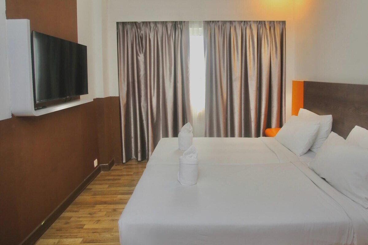A hotel room with a large bed, a flat-screen TV mounted on the wall, and a window with curtains.